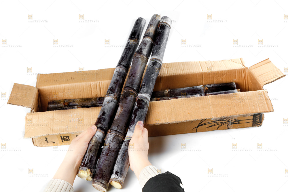 白底上一箱黑皮甘蔗和手上拿着甘蔗